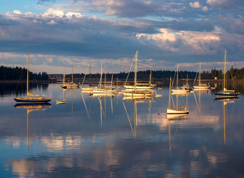Boats moored in a calm harbor, reflected in the water at sunset