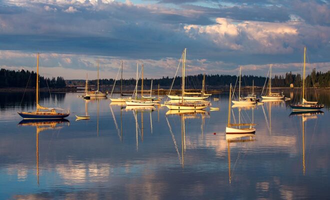 Boats moored in a calm harbor, reflected in the water at sunset
