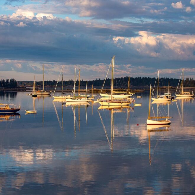 Boats moored in a calm harbor, reflected in the water at sunset