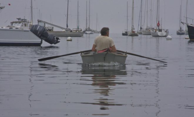 Gray, a lobsterman feathers his oars along the surface of Rockport Harbor.
