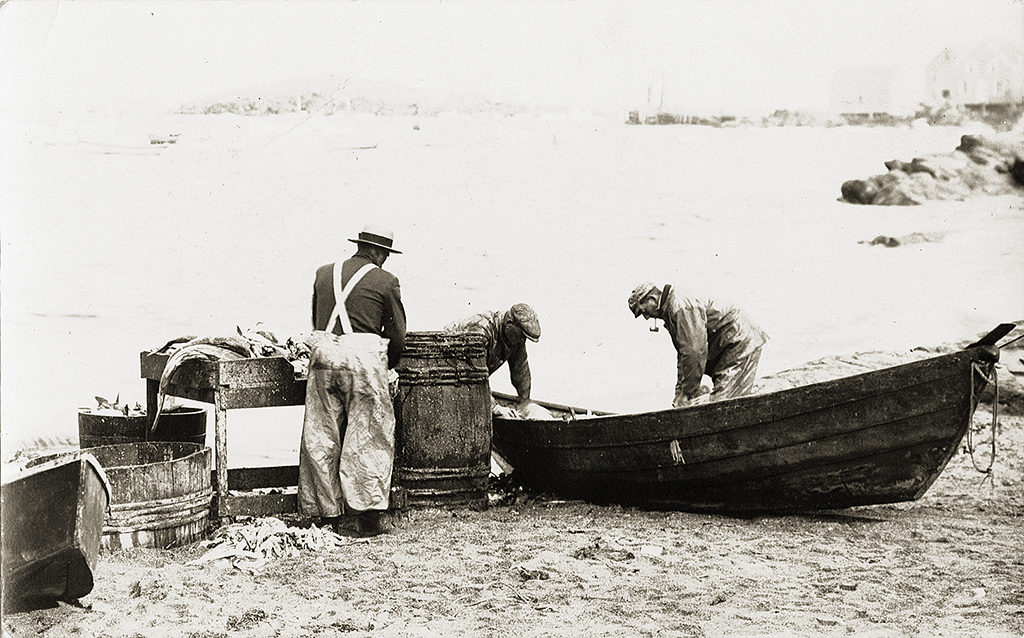 Monhegan Island, Maine — Fishermen cleaning catch out of a dory on the beach. From a postcard