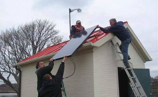 Crews install solar panels on the Pomham Rocks Lighthouse's oil house. The power generated will be used in a security system.