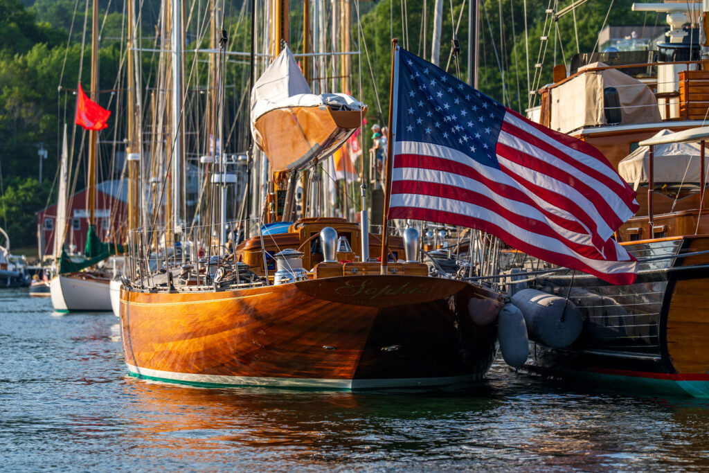 A sailboat with sunlight reflecting off the hill and an American flag flying off the stern