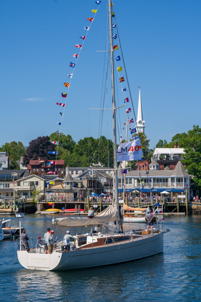 sailboat with flags in a harbor and a white steeple in the background
