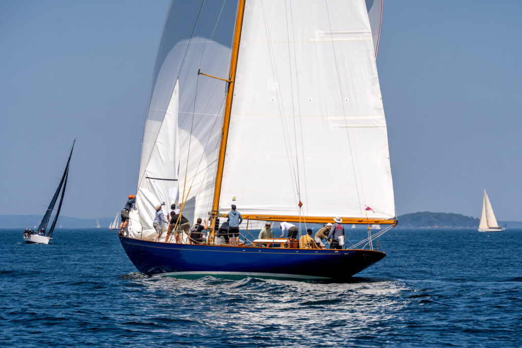 A blue sailboat with the crew changing the sails