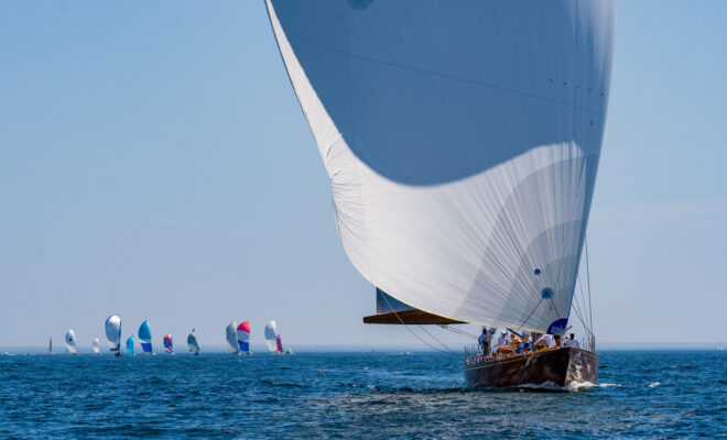 A sailboat leads the fleet on a downwind leg. Spinnakers flying
