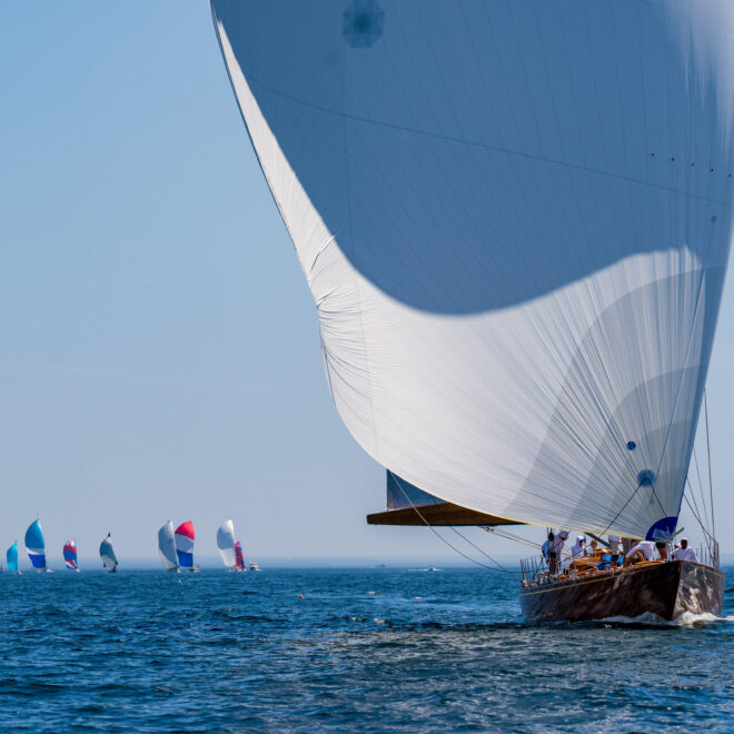 A sailboat leads the fleet on a downwind leg. Spinnakers flying