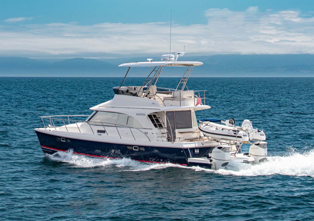 Power catamaran with a flying bridge underway with outboard motors and a tender mounted on the aft of the boat.