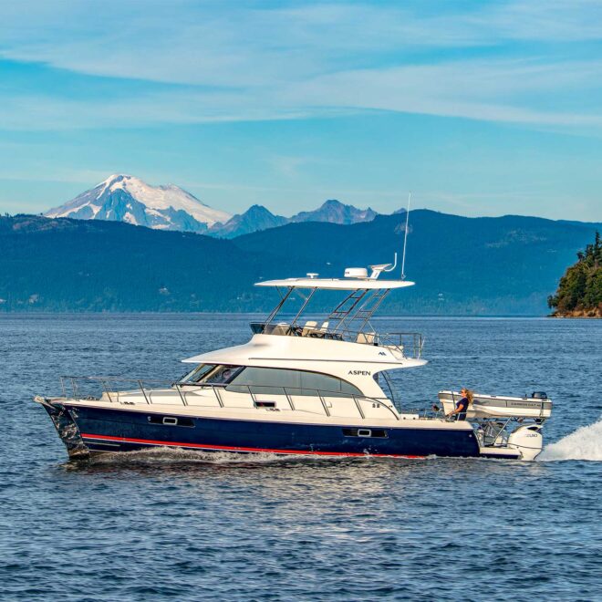 aspen catamaran running along the coast of washington state with snow-capped mountains in the distance.