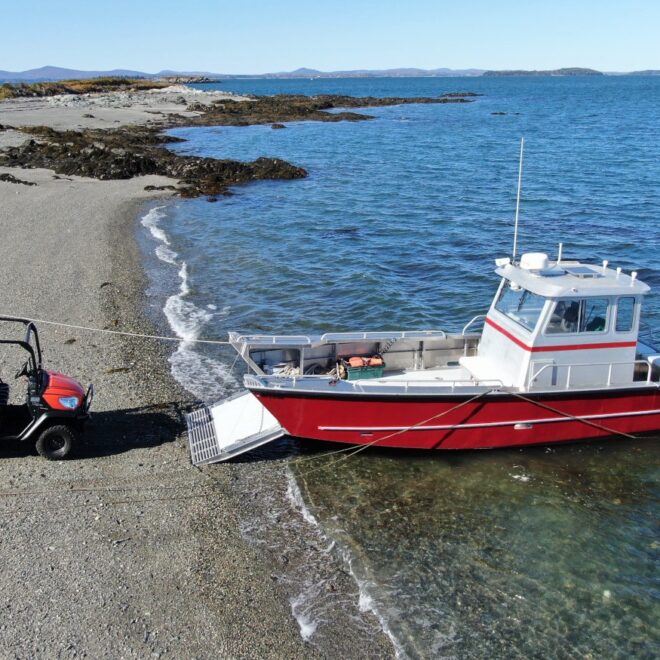 A red aluminum landing craft beached, a four-wheel vehical unloaded on the beach.