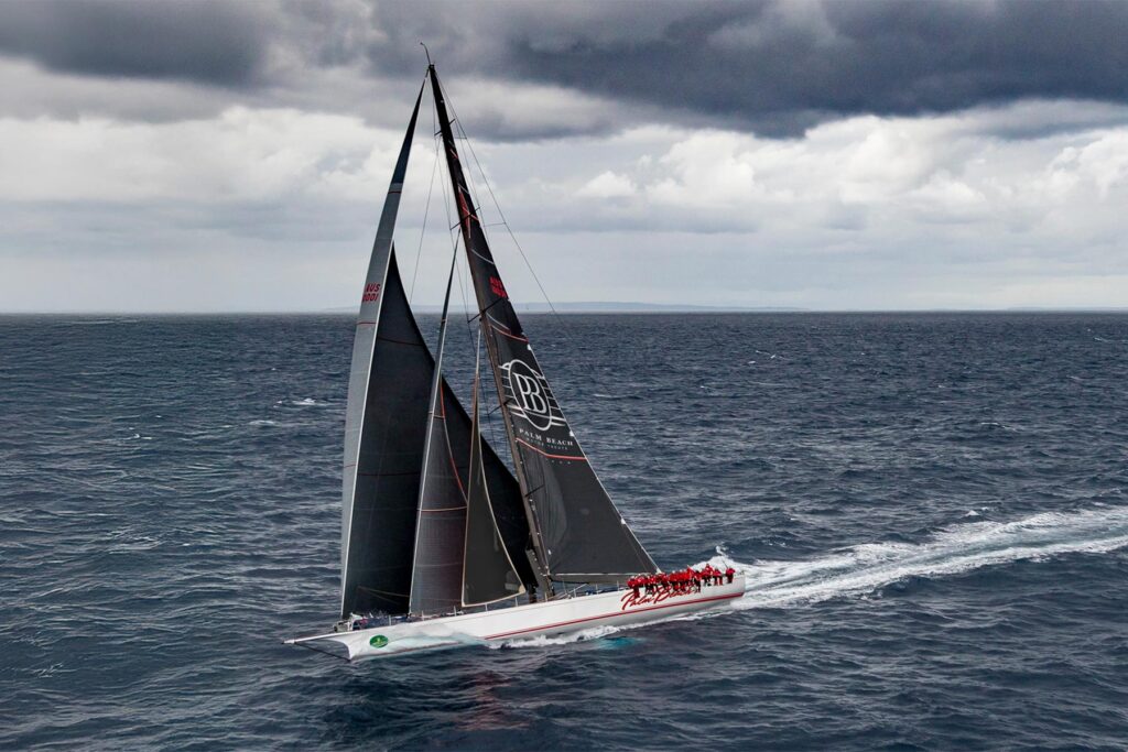 a large sailboat underway with the crew sitting on the rail