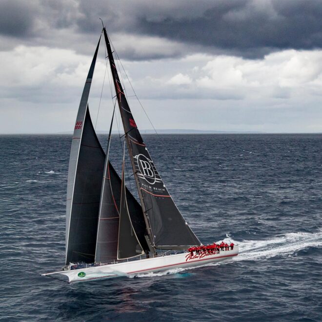 a large sailboat underway with the crew sitting on the rail