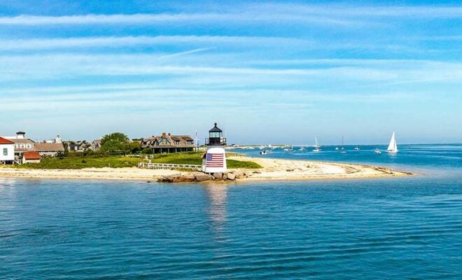 Sailboats sailing near Nantucket Harbor Lighthouse with an American Flag