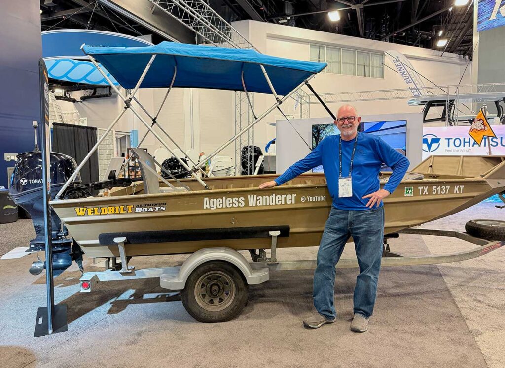 A man wearing a blue shirt standing next to a boat on a trailer