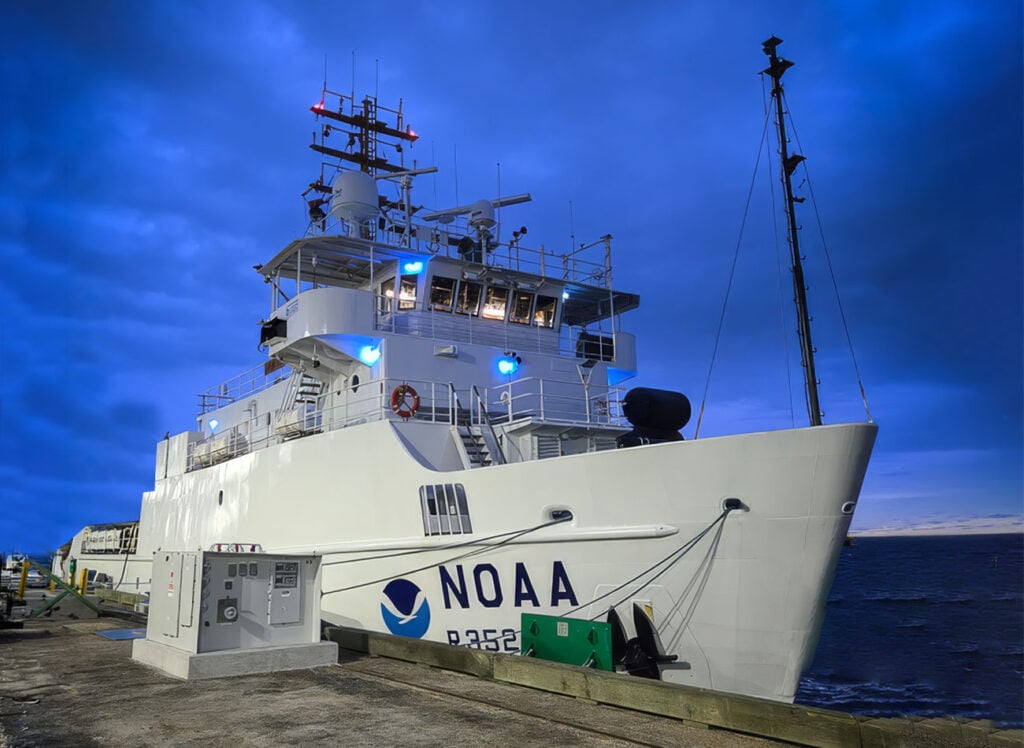 NOAA Ship Nancy Foster docked. Dock lights illuminate the ship, light in the sky fades just after the sun has set.
