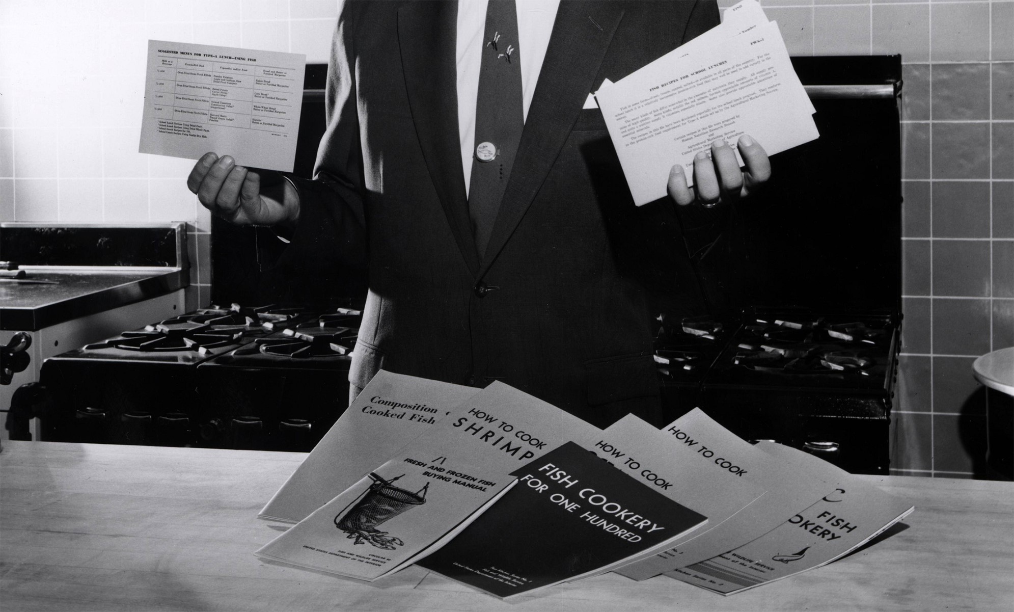A man shows off Test Kitchen recipe cards for a program at Maryland, College Park BCF laboratory. (Image credit: NOAA Central Library Historical Fisheries Collection)