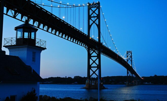 A lighthouse stands at the base of the Bristol Mount Hope Bridge dark blue sky at dusk in Rhode Island