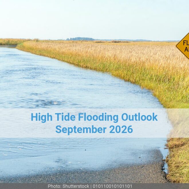 A road sign that reads flood area on a road that is completely flooded and lined by a field on both sides