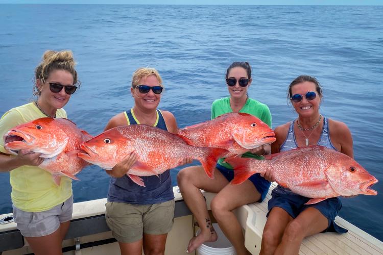 A group of women aboard a boat hold large red snappers caught during a recreational fishing trip. Credit: Grayson Shepard
